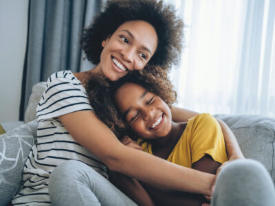 Mother embracing her cute daughter on the sofa at home