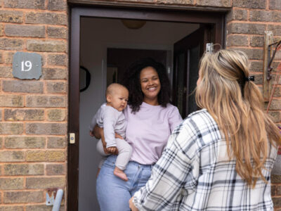 Woman with baby answering her apartment door to a friend