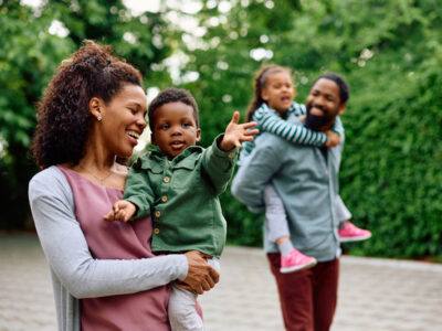 Happy woman holding her small son while walking outdoors. Father and daughter are in the background.