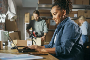 Woman business owner in warehouse at desk with computer