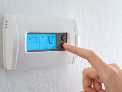 Hand pressing indoor room thermostat to lower the temp