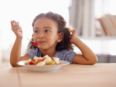Shot of a cute little girl eating fruit salad at a table