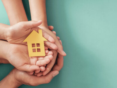 Hands holding yellow paper house on blue background