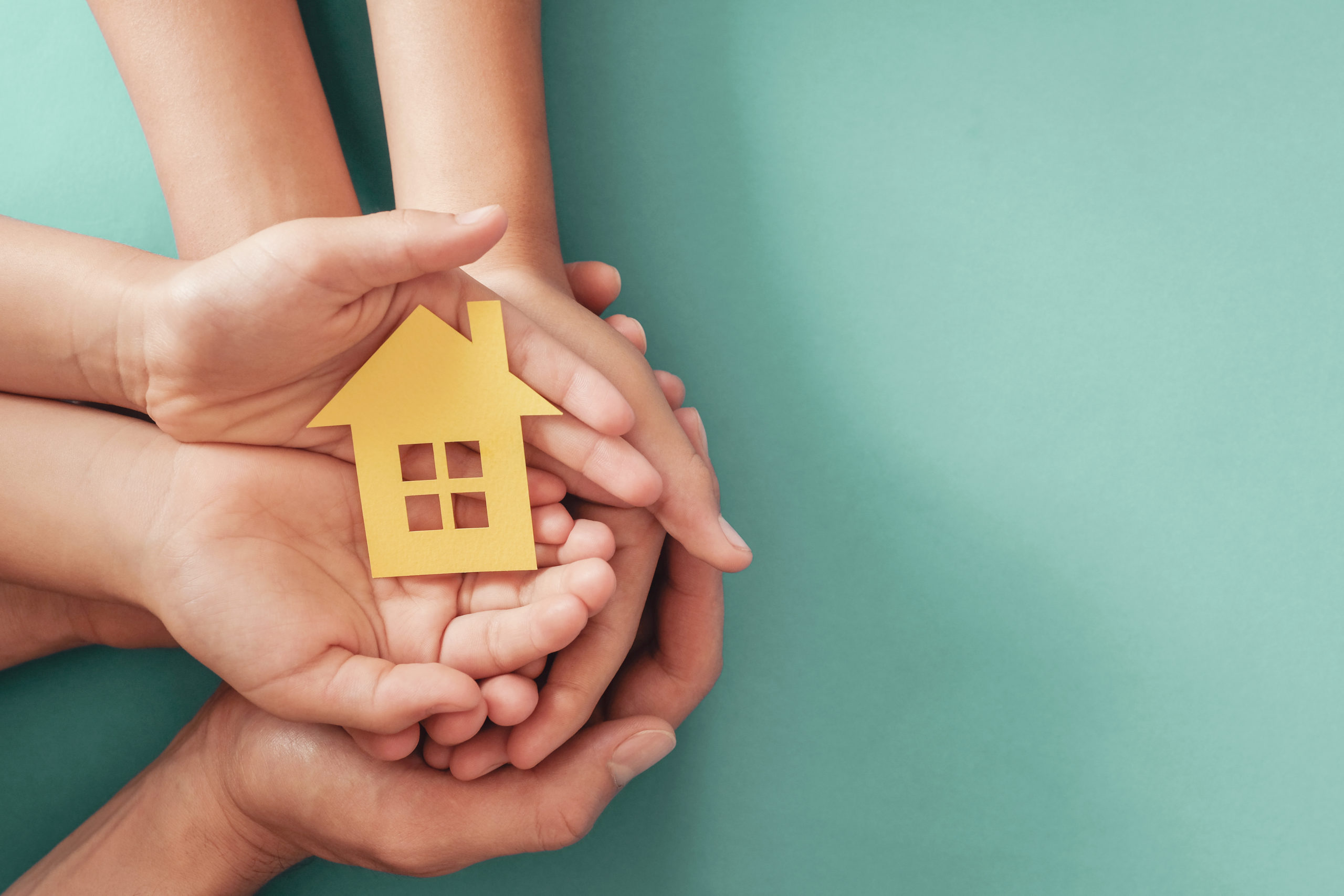 Hands holding yellow paper house on blue background